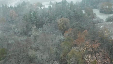 High-angle-aerial-of-a-snow-storm-falling-over-an-autumnal-woodland-in-Canada