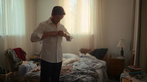 man buttoning his shirt in a bedroom