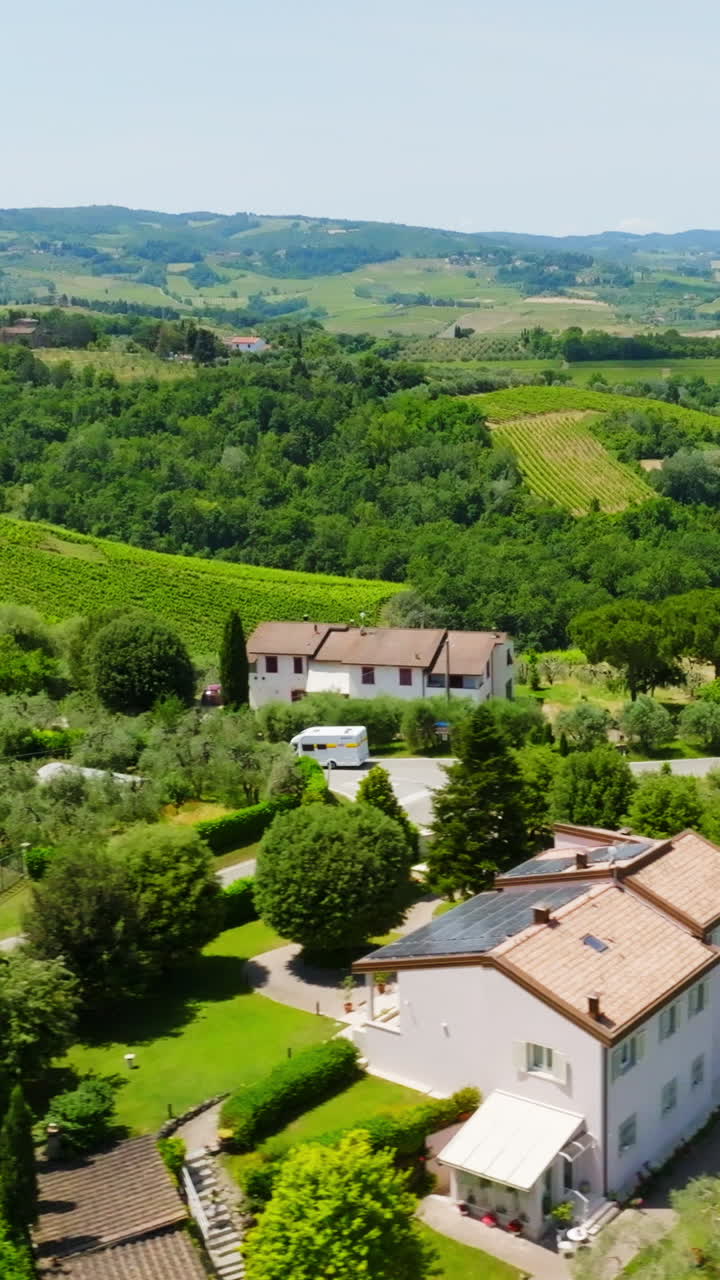 Vertical drone shot following a RV driving between vinyards and a Tuscan town