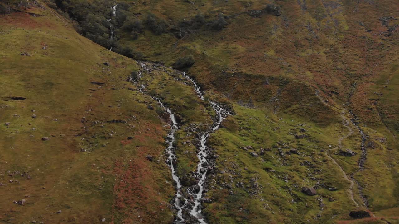 retirada aérea de un río que corre hacia abajo por una ladera escocesa en las tierras altas de glencoe, escocia