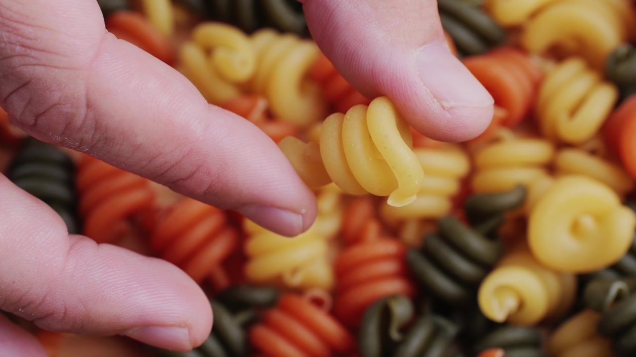 Close-up of Hand Holding and Dropping Uncooked Tri-Color Spiral Pasta