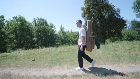 junger mann geht mit gitarre auf der straße in der nähe des waldes
