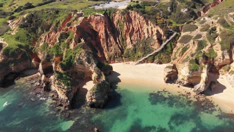 Camilo-Beach-encircled-by-steep-sandstone-cliffs-in-Lagos,-Algarve,-Portugal---Aerial-Wide-Slow-Orbit-shot