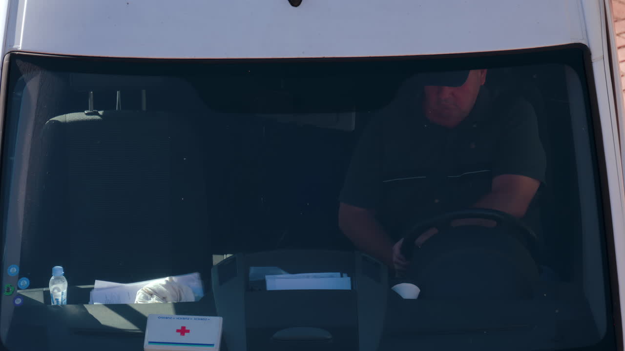 Chisinau, Moldova - September 28, 2025: A man in a dark shirt driving a van under direct sunlight, viewed through the windshield