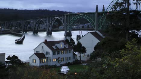 Los-Automóviles-Y-Otros-Vehículos-Viajan-A-Través-Del-Puente-De-Newport,-Oregon,-En-Una-Mañana-Tranquila-Y-Pacífica,-La-Estación-De-Guardacostas-En-Primer-Plano-En-El-Antiguo-Frente-Histórico-De-La-Bahía-En-La-Costa-De-Oregon