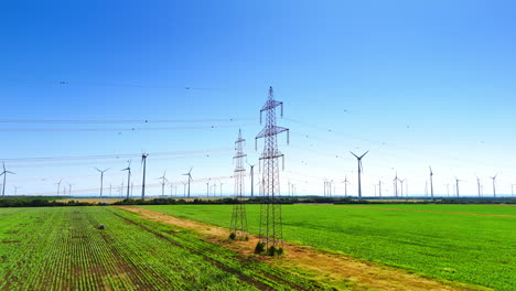 green agricultural fields with power lines. wind turbines slowly rotate in the wind at backdrop