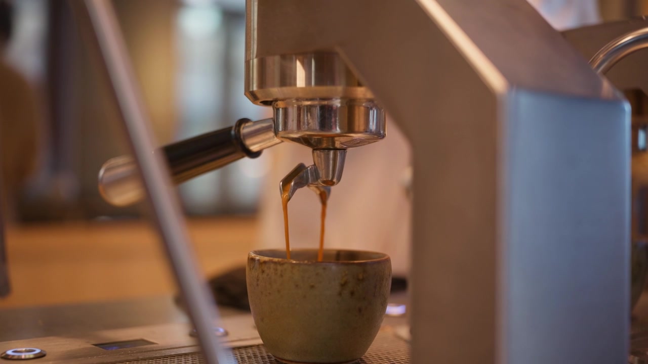 Un primissimo piano mostra un ricco espresso che scorre dal portafiltro di una macchina in una piccola tazza di ceramica, perfetto per contenuti di branding per caffè e caffetterie