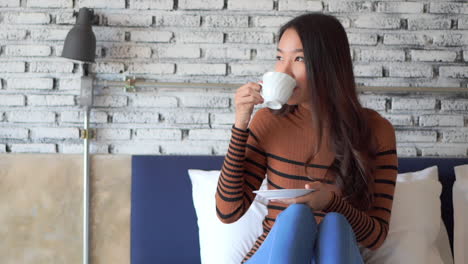 Charming-asian-woman-relaxing-on-sofa-holding-cup-of-tea