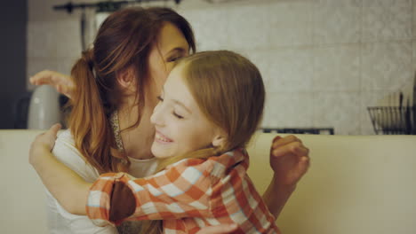 young pretty mother in the apron putting a plate with muffins on the kitchen table in front of her happy daughter. indoors