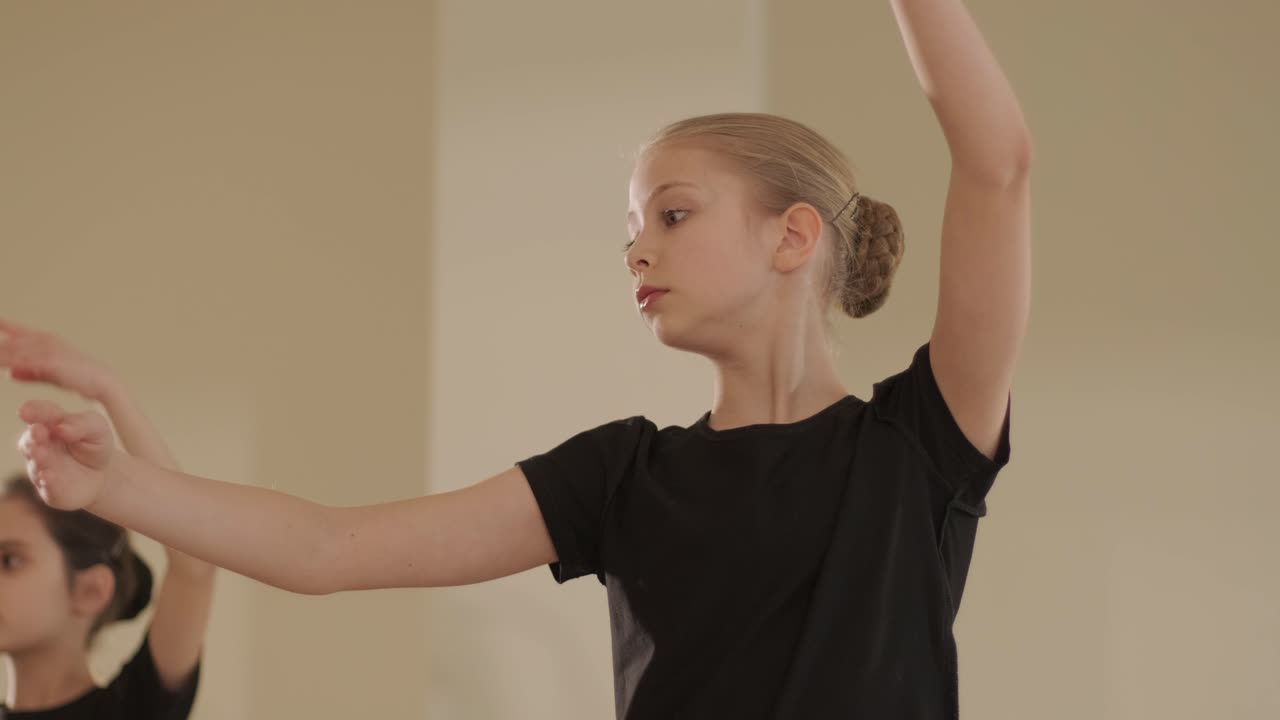 un grupo de jóvenes estudiantes de ballet con ropa de baile negra practicando posiciones en un amplio estudio de ballet con pisos de madera y barras montadas en la pared. expresiones enfocadas y movimientos sincronizados.
