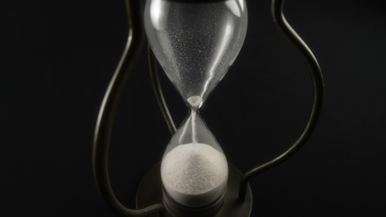 White Sand Flowing Through an Hourglass on a Black Background