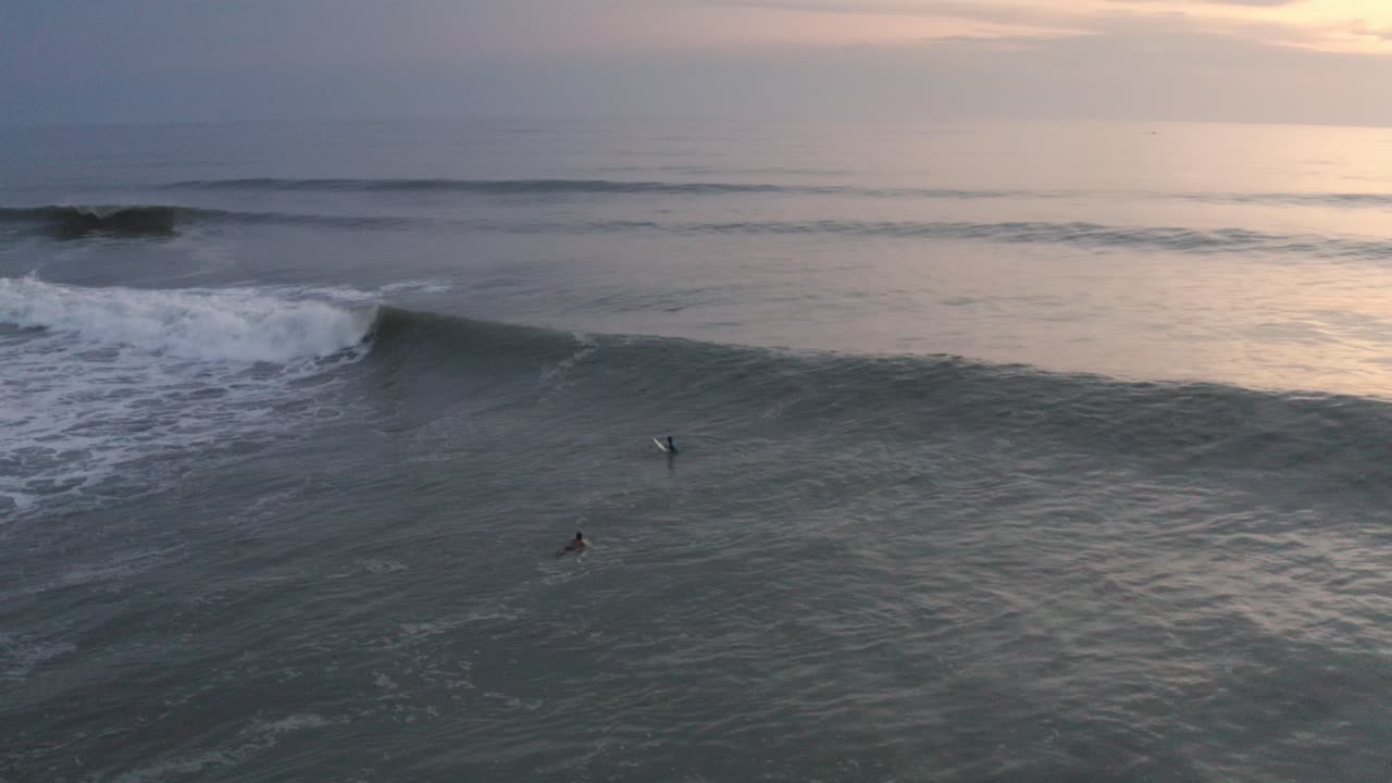 Surfisti che remano sulle onde nelle acque costiere, vista aerea al tramonto.