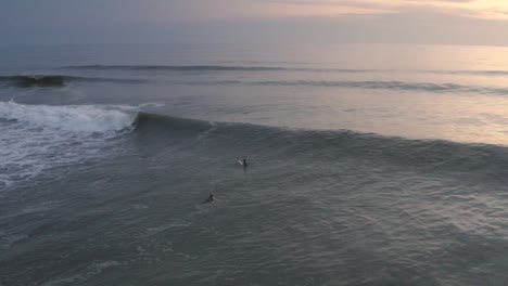 surfers paddling over waves in coastal waters, sunset aerial view