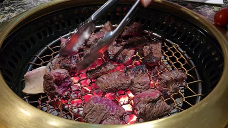 a sizzling korean bbq grill at hanu beef restaurant, chef flips juicy raw beef cube pieces of meat, pineapple, chili, and tomato, cooked over glowing charcoal for a flavorful dining experience