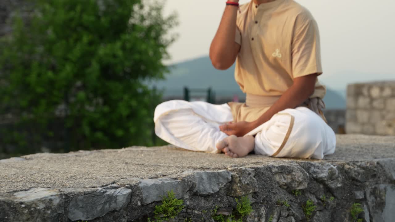 인도 남성이 돌 위에 앉아서 해가 뜨는 새벽에 명상을 하고 있는 장면