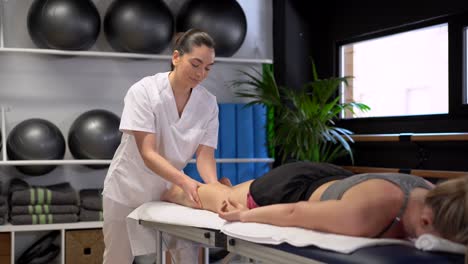 anonymous female physiotherapist massaging leg of crop woman