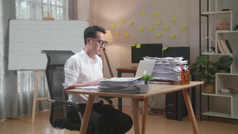 hombre asiático haciendo una llamada de video en una computadora portátil mientras trabaja con documentos en la oficina