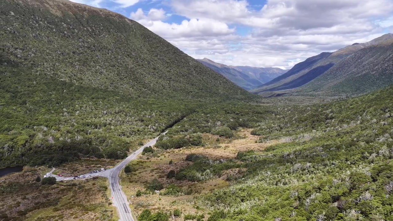 Veduta aerea di una strada tortuosa attraverso una valle verde lussureggiante e montagne sotto un cielo nuvoloso