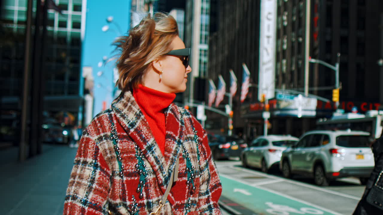 New York, USA, 5 ottobre 2025: Primo piano di donna con occhiali da sole in una strada di New York. Ritratto di donna che indossa occhiali da sole e un cappotto a quadri rosso mentre cammina lungo una strada a Manhattan, New York.