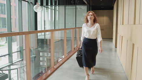 A-red-haired-young-businesswoman-walks-backwards-with-a-trolley.-She-is-on-his-way-to-an-important-business-trip.