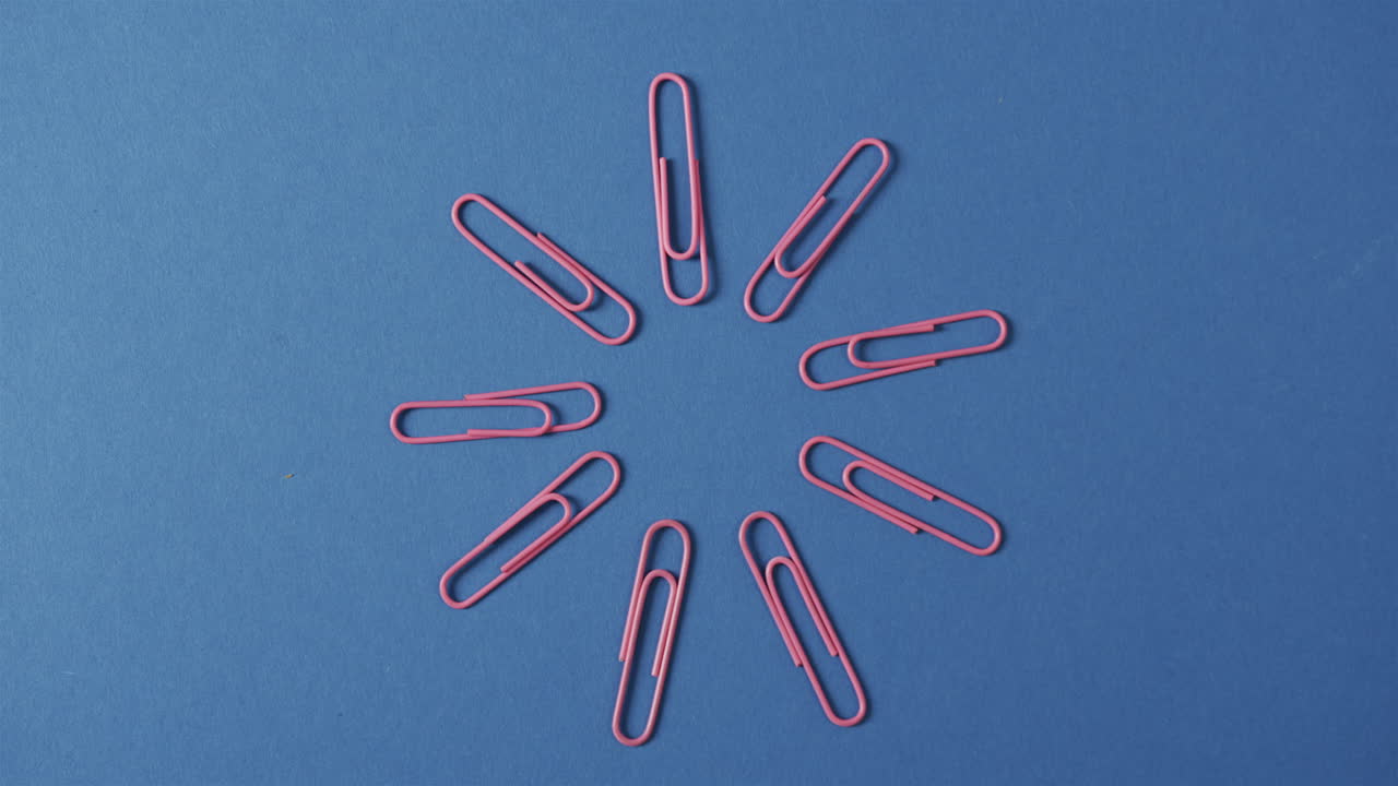 Overhead view of pink paper clips arranged on blue background, in slow motion