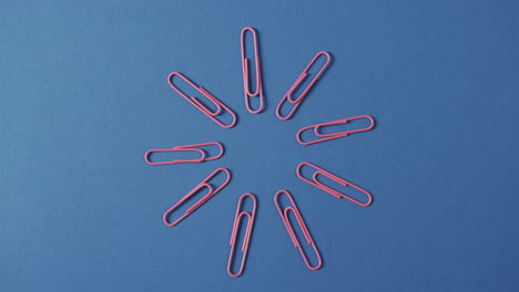 overhead view van roze paperclips gerangschikt op blauwe achtergrond, in slow motion