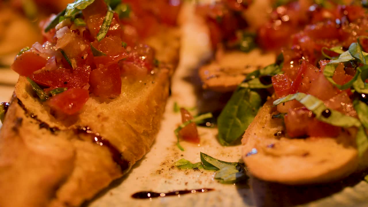 Camera slowly pans across toasted bruschetta topped with tomato, basil, balsamic, and olive oil