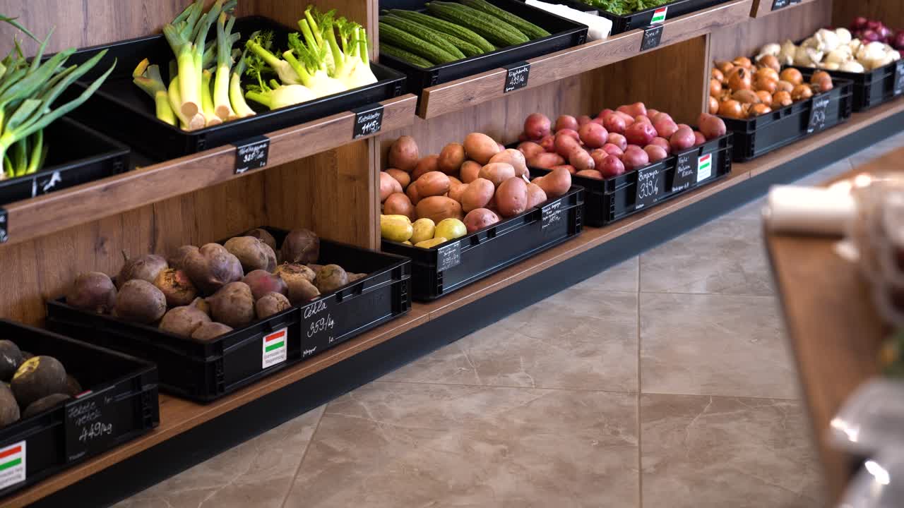 Variety of vegetables in bins, for sale in market, slow pan, left to right.