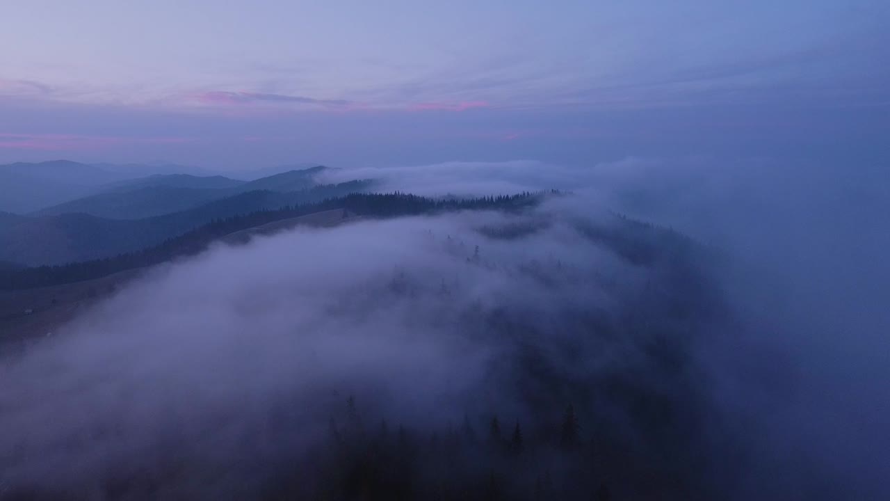Beautiful aerial view of misty mountain valley scenery with village from a drone flying forwards on misty morning in Carpathian Mountains, Romania. Cinematic drone shot of countryside scene in morning