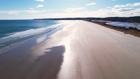 Beach-flyover-into-a-bright-sunny-sky-with-tides-on-the-sand-and-waves-crashing