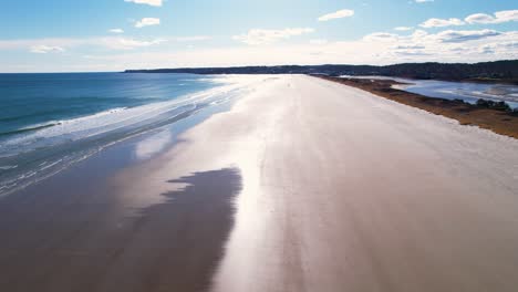 beach flyover into a bright sunny sky with tides on the sand and waves crashing