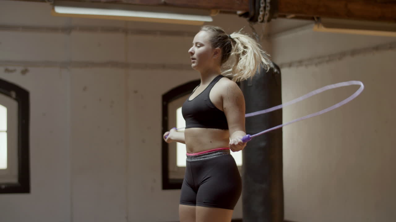 Medium shot of focused Caucasian woman jumping rope in gym