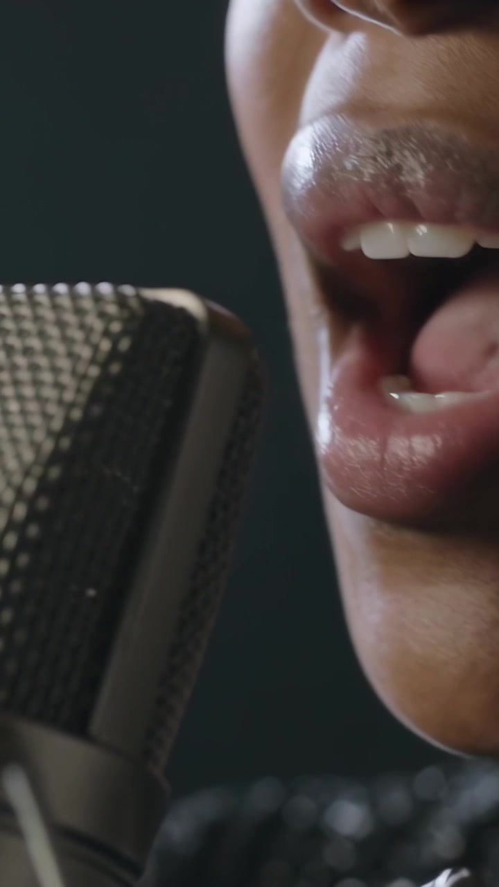 Video verticale: Un cantante articola i suoni in studio, con un grande microfono e un top scuro.