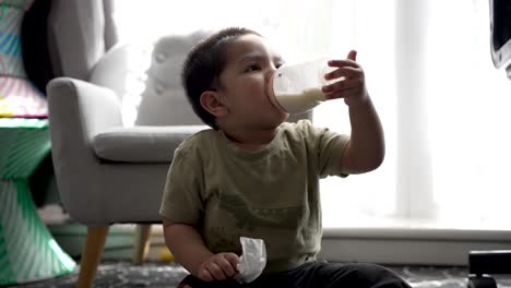 South-Asian-UK-18-Month-Old-Toddler-Boy-Drinking-Milk-While-Sitting-On-The-Floor-At-Home-Being-Joyful-And-Cheeky