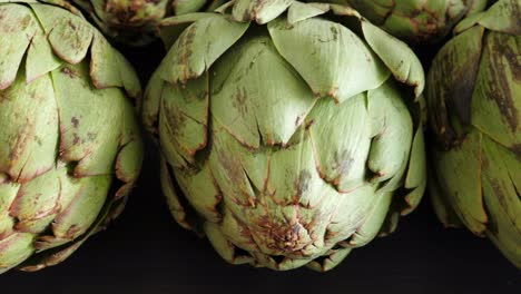 Whole-fresh-artichokes-on-black-table,-closeup