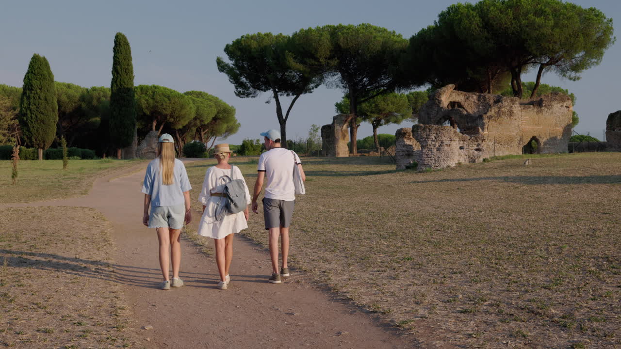 Familie går langs en sti i Appia Antica Park i Rom med antikke ruiner og pinjetræer i varmt aftenlys