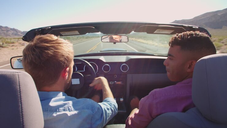 Due uomini in auto cabriolet che guidano lungo una strada, ripreso con R3D