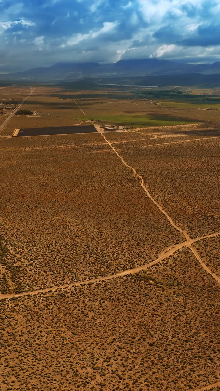 Descending over the dry desert in Death Valley. Some houses are built around the highway crossing the landscape. Vertical video