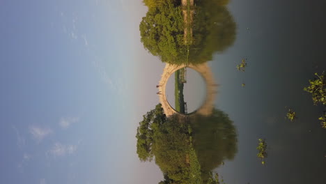 formato vertical: antena baja a puente de arco de piedra reflejado en estanque