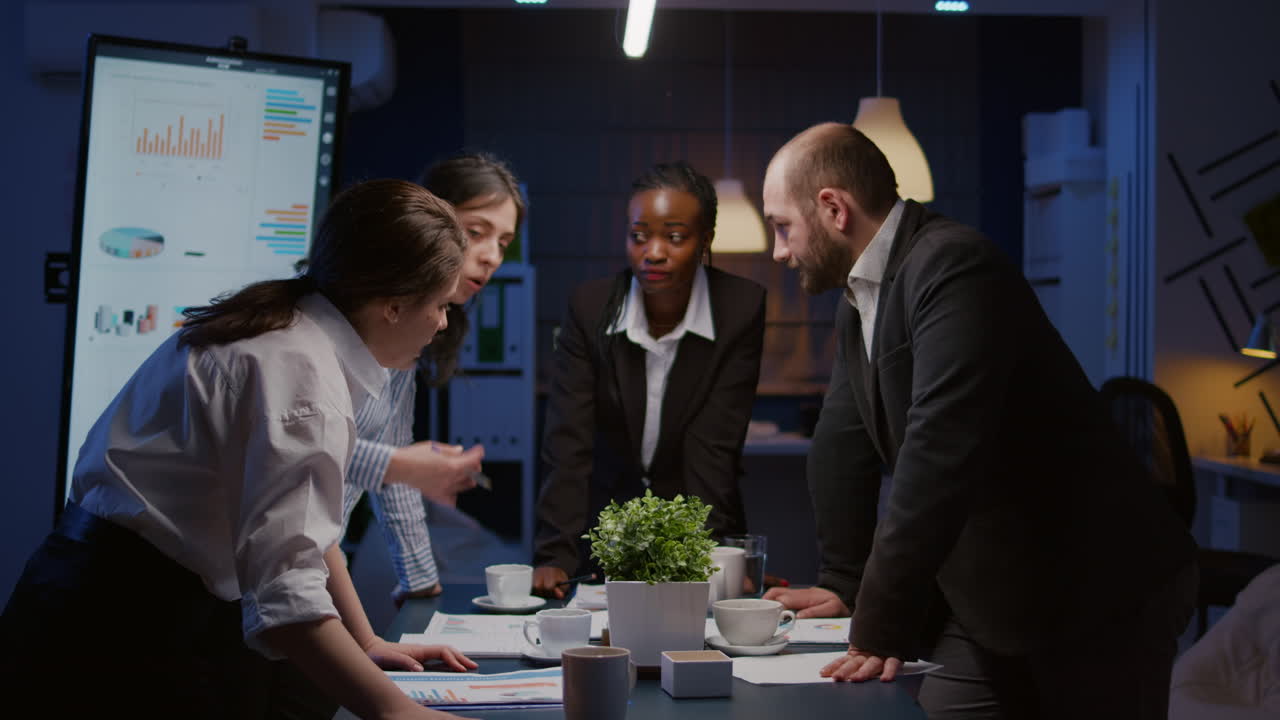 Diverse multi ethnic businesspeople discussing over graphs paperwork standing at conference table