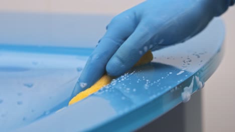 A-woman-in-blue-rubber-gloves-cleans-the-table-with-a-sponge-with-a-foaming-detergent