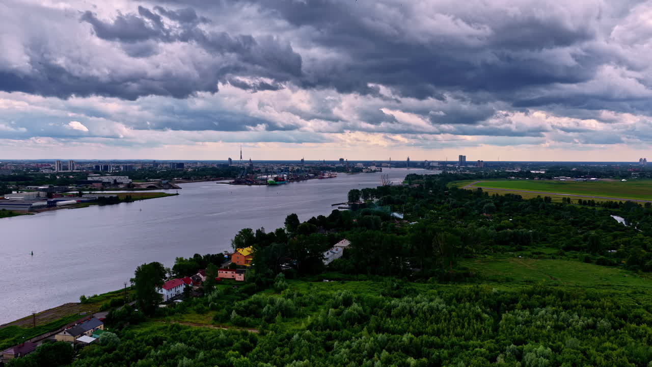 Dark storm clouds loom above the Daugava River, rural homes, and Riga's skyline in the distance. Riga, Latvia