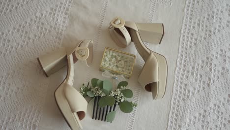 pair of beige high-heeled shoes with floral hair accessory and jewelry box on white lace fabric