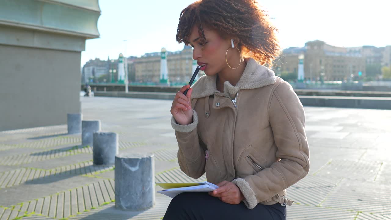 Woman with curly hair writing in a notebook in the city