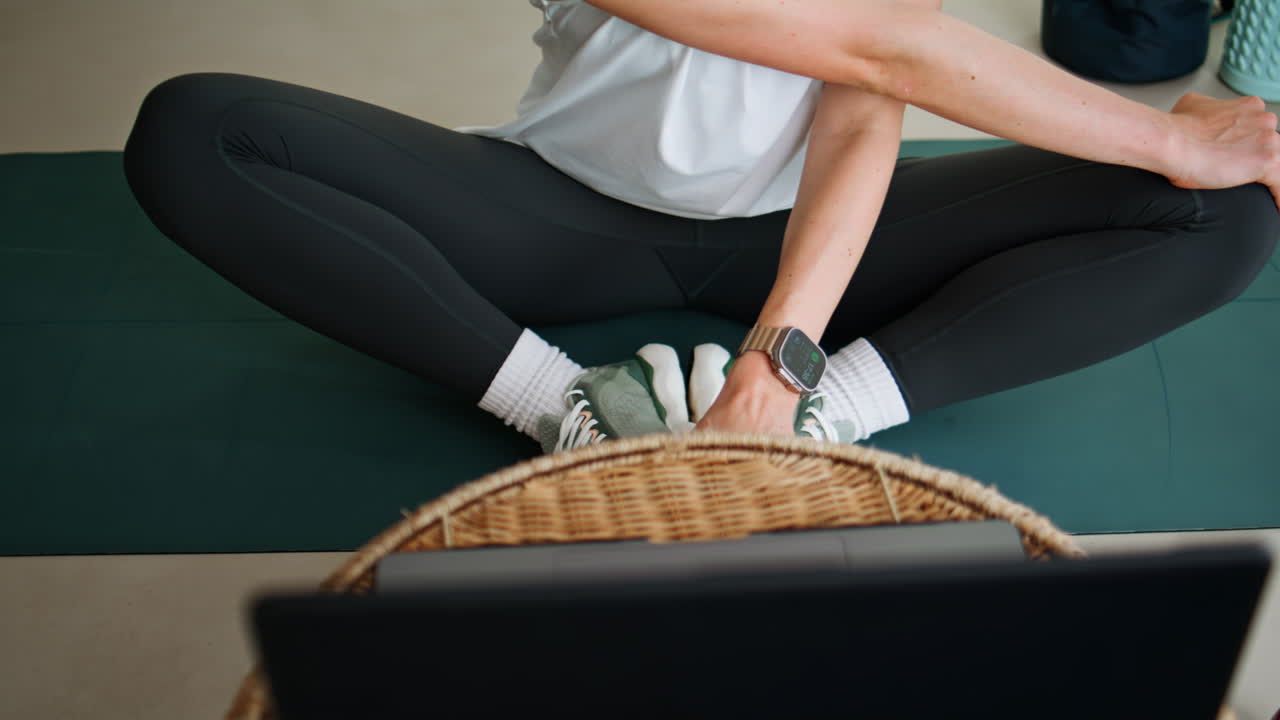 Unknown woman sitting cross-legged on yoga mat watching laptop closeup