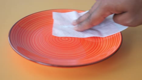 close-up of a hand wiping a red plate with a paper towel