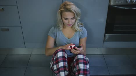 mujer encantadora con smartphone en el suelo de la cocina