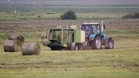 un tractor con un remolque para hacer balas trabaja en el campo y recoge rollos de paja o alimento