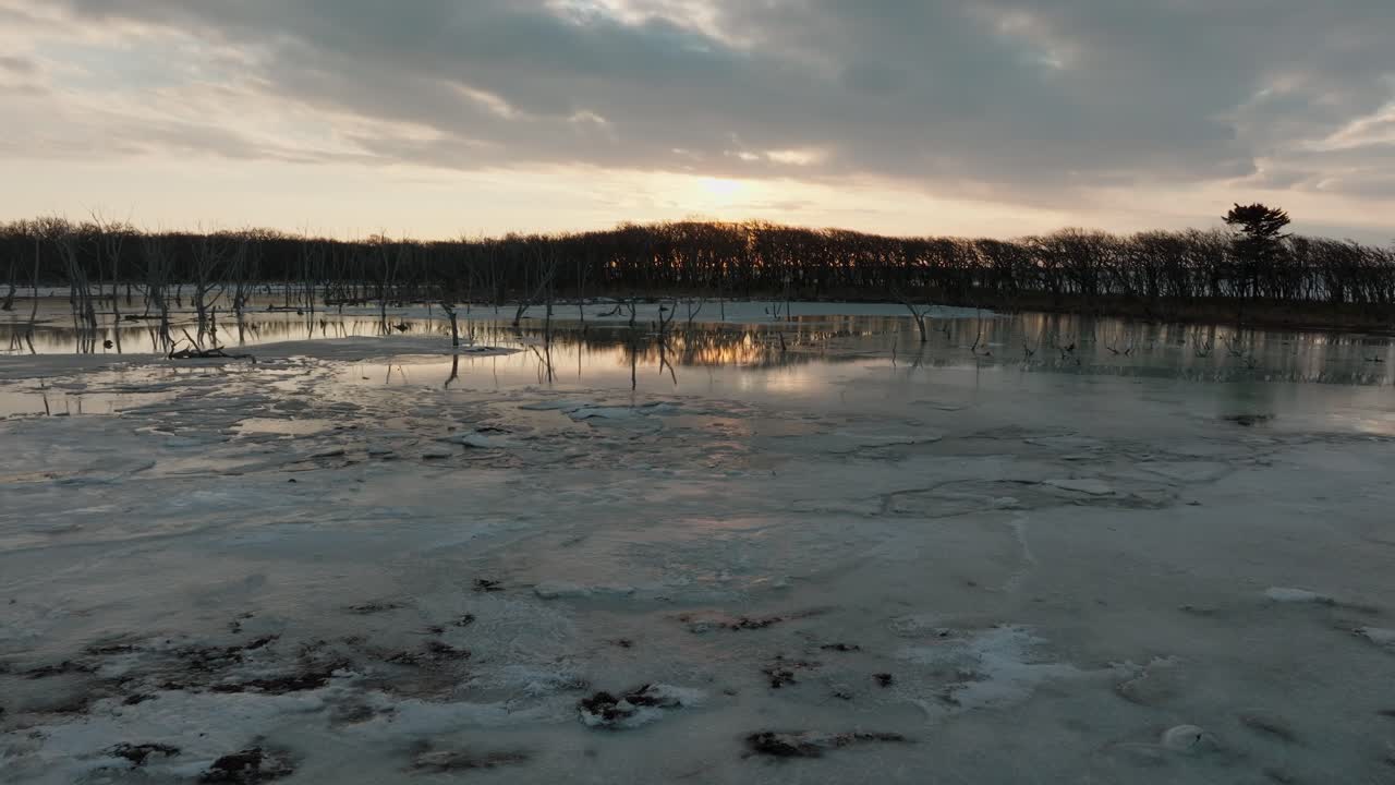 Sunrise Sky Reflections On Partially Frozen Lagoon With Woods In Notsuke Peninsula, Hokkaido, Japan. wide drone shot