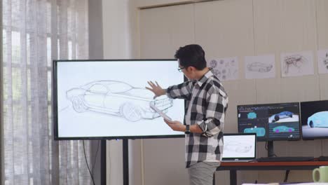 asian male comparing his design to the photo on tv while working on car design sketch in the studio with computers display 3d electric car model